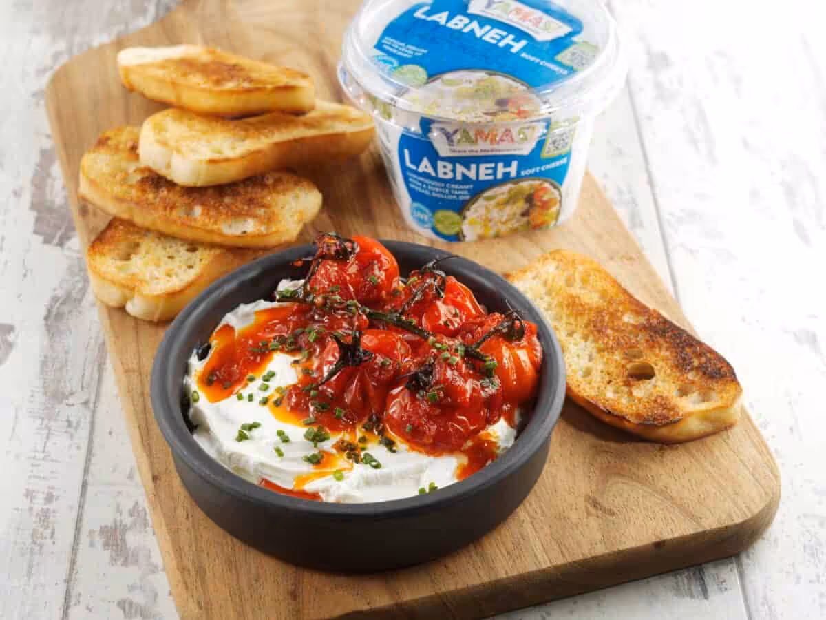 YAMAS! Labneh in a dark bowl topped with harissa roasted tomatoes and toasted ciabatta