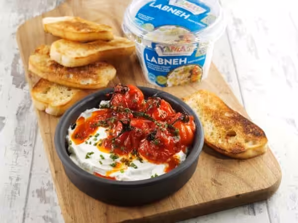 YAMAS! Labneh in a dark bowl topped with harissa roasted tomatoes and toasted ciabatta